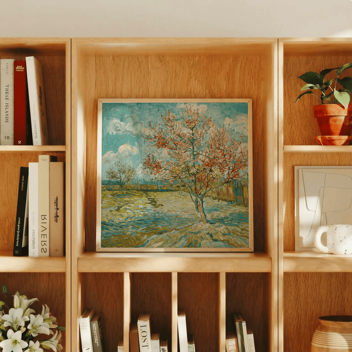 Framed print of impressionist wall art showing a flowering tree and sky on a wooden shelf with books and a plant
