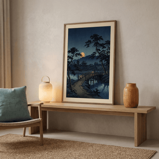 Moonlit Bridge Art Print leaning on a wooden bench with a lamp and pottery in a neutral room