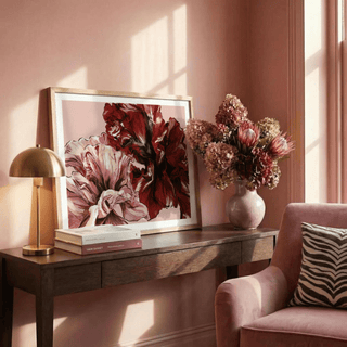 Pink floral print leaning on a wooden table with books and a vase of flowers in a softly lit room