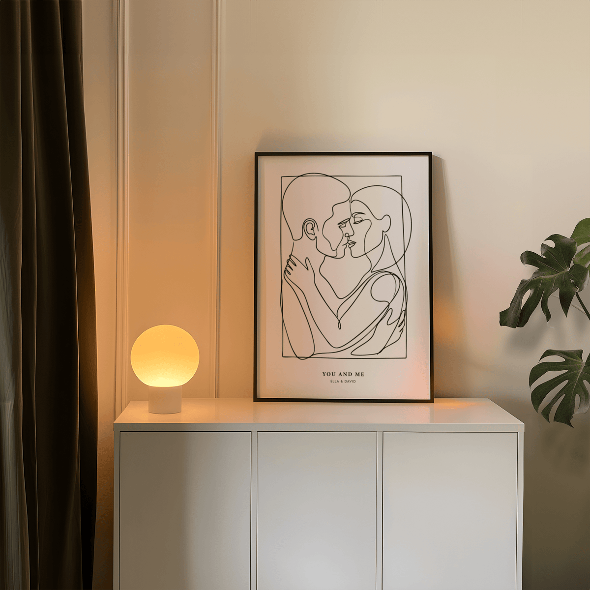 Abstract Figures print with embracing couple line-art in black and white on a sideboard with a round lamp and plant