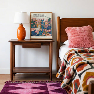 Mexican wall decor print on a bedside table with an orange lamp and pink cushion