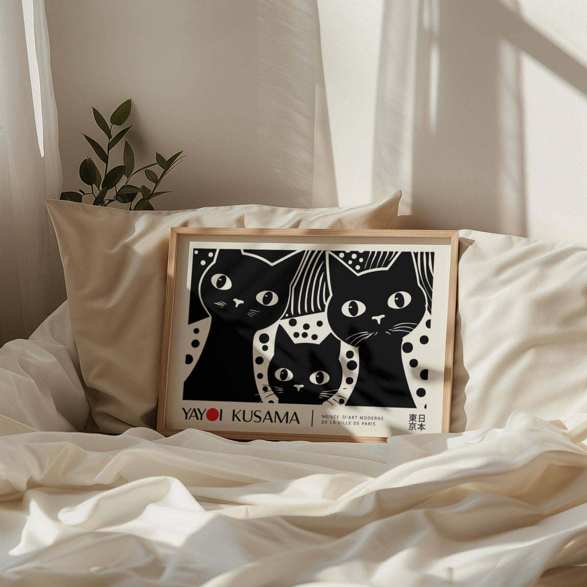 Framed Black Cat Wall Art print with minimalist black cat faces and off-white background placed on white bedding with a green plant