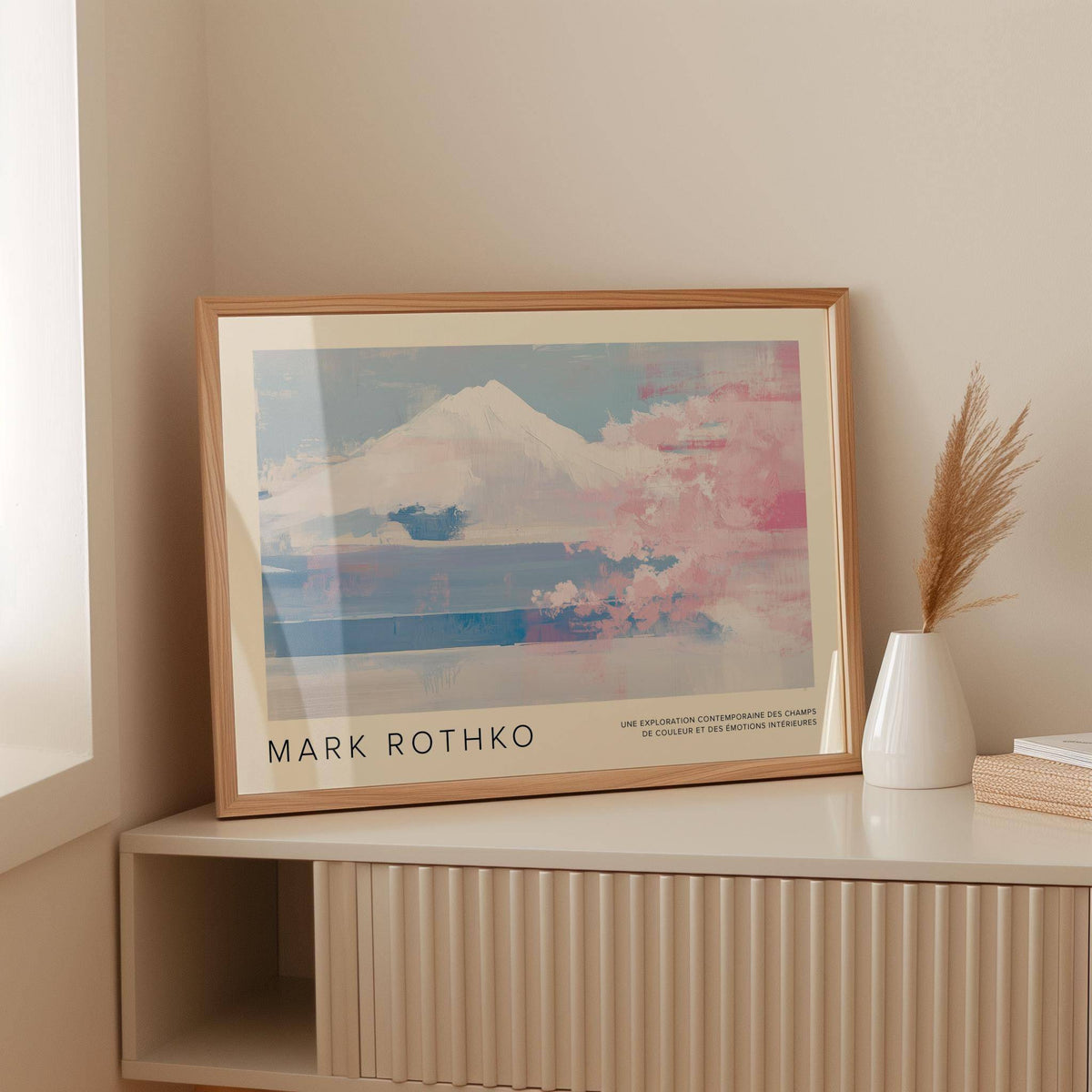 Framed mountain landscape wall art with pink cherry blossoms leaning on a cabinet with a white vase
