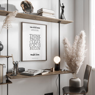 Print on a wall of motivational art for the office with black typography above a desk with a lamp and pampas grass
