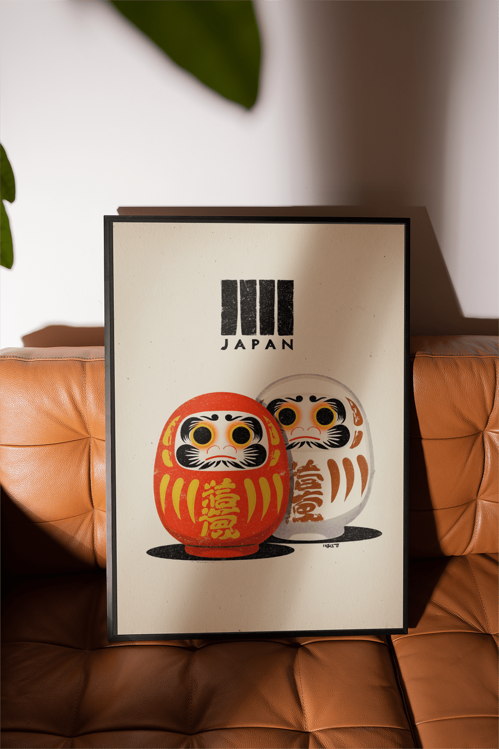 Framed Daruma Print with red and white daruma dolls on a brown leather seat