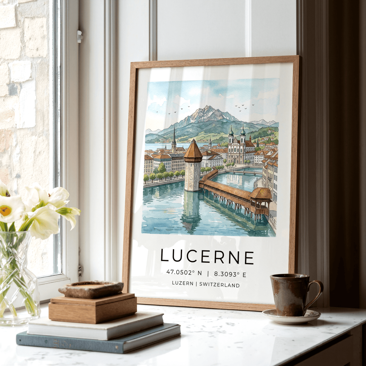 Lucerne Watercolor Art Print leaning on a windowsill beside books and a brown cup with natural light