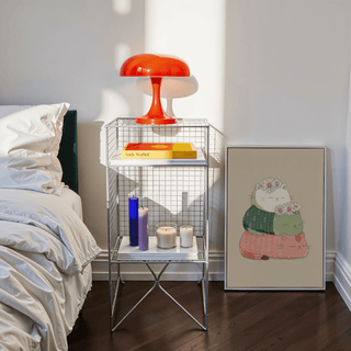 Cute Cat Art Print leaning against a wall near a bedside table with colourful candles and a red lamp