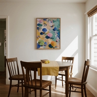 Beach Umbrellas Print hanging above a dining table with four wooden chairs and a window to the right