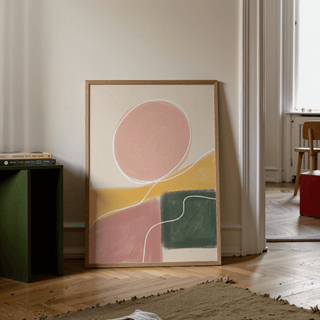 Modern Abstract Print leaning on a wooden floor with muted pink circle and green and yellow shapes in a softly lit room