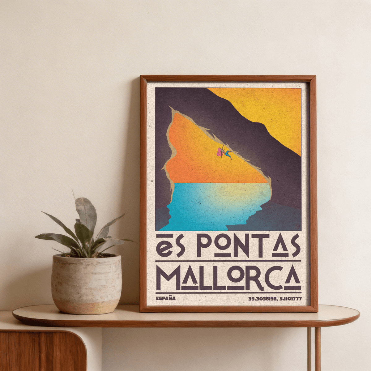 Framed Mallorca Climbing Poster of a climber on a cliff in orange yellow and blue hues leaning on a wooden table with a plant