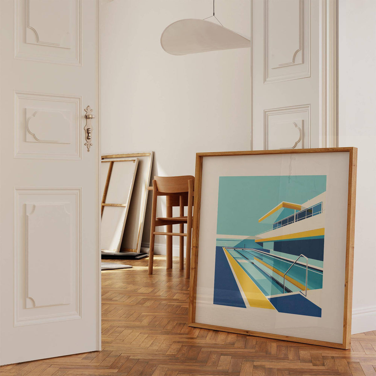 Print leaning on a floor showing modern poolside art in a minimalist style with blue and yellow shades in a room with wooden flooring