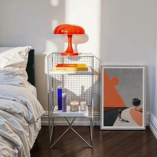Cycling Landscape Art Print leaning on floor next to a metal side table with a red lamp in a bedroom