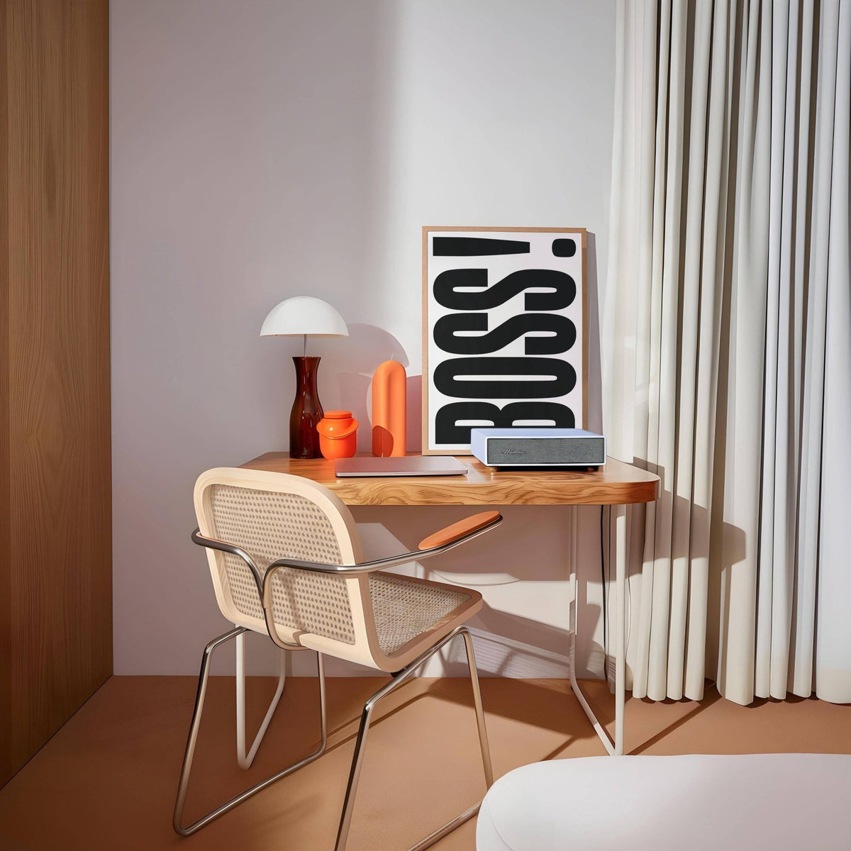 Print leaning on a wooden desk with boss typography in black and white and a red-orange glass vase nearby in a room with curtains