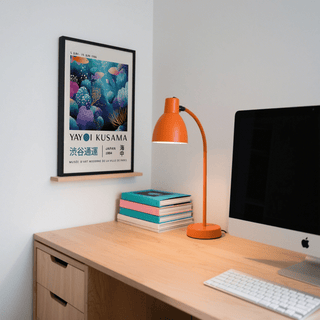 Fish artwork prints in a light wood frame showing colourful coral reef and fish above a wooden desk with an orange lamp