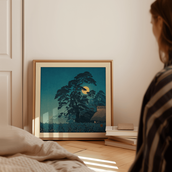 Framed Hasui Kawase Moon Print leaning by a stack of books with green and yellow tones