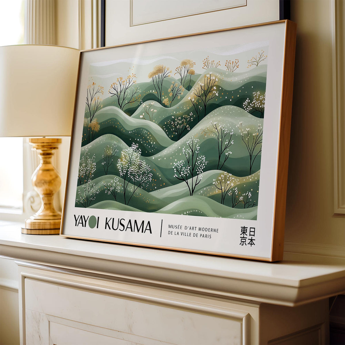 Framed Landscape Art Prints of hills with blossoming trees in soft green and beige tones leaning on a mantelpiece next to a lamp