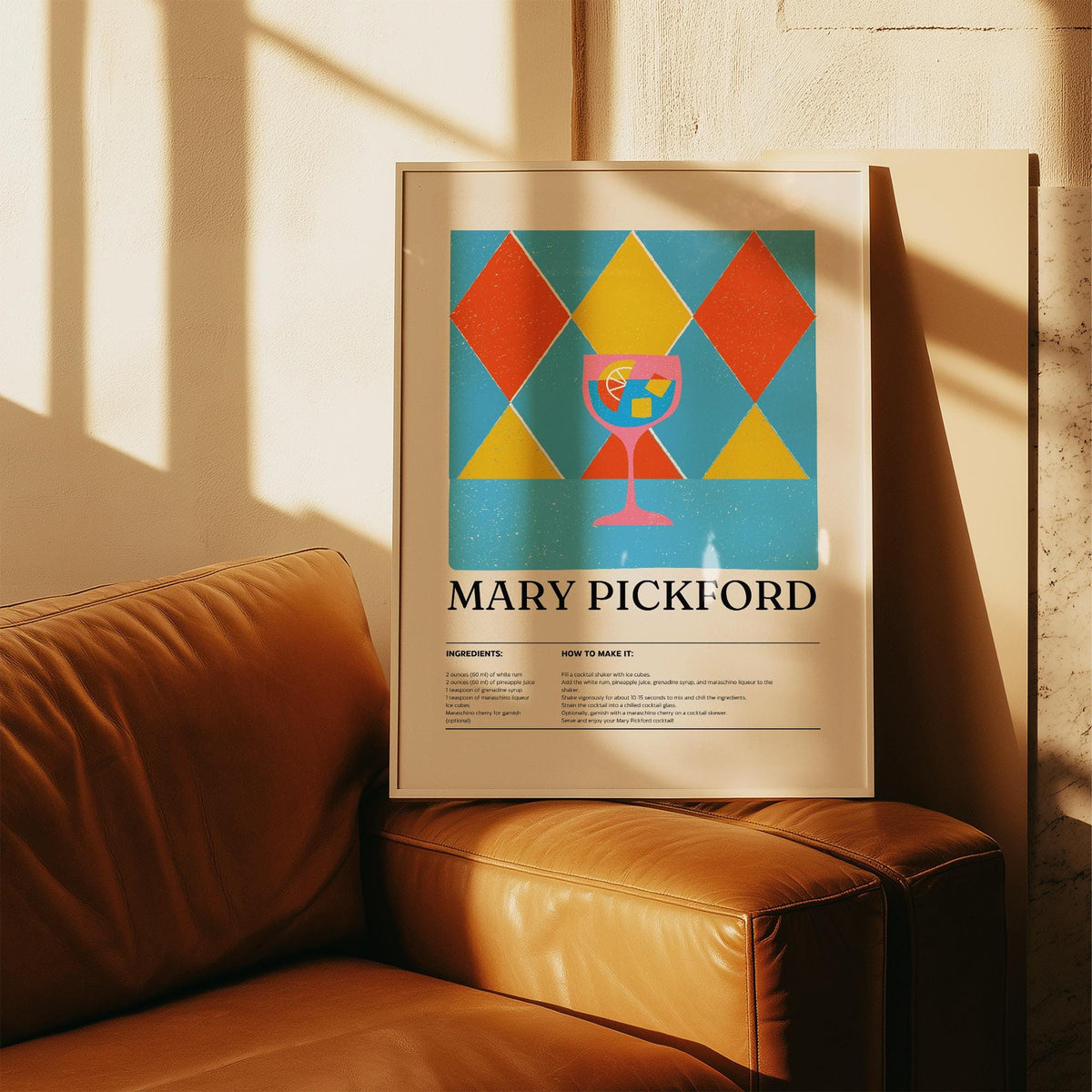 Framed print of a pink cocktail glass with geometric red and yellow diamonds leaning on a leather couch