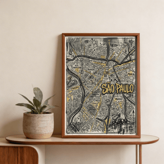 Framed Sao Paulo Map Art graffiti cityscape in black and gold colours resting on a wooden shelf beside a potted plant
