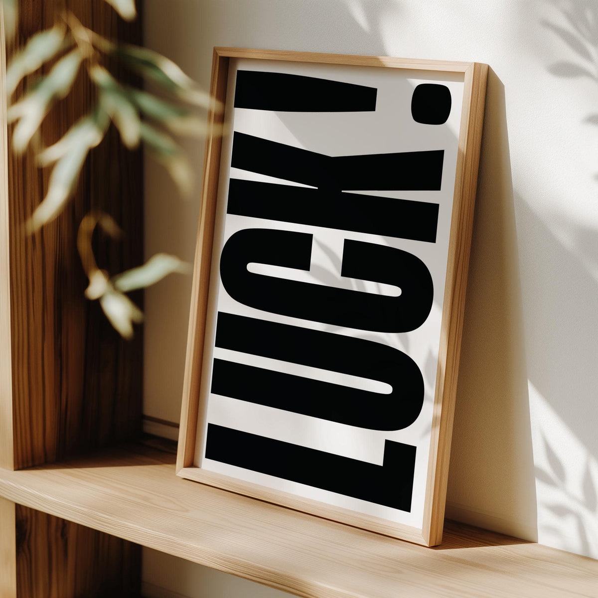 Framed Good Luck Print leaning on a wooden shelf with black bold typography and white background