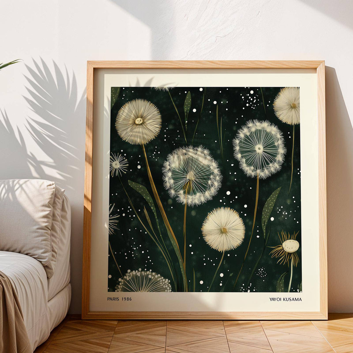 Square wall art of white dandelion seed heads on dark background leaning on floor near a cream sofa