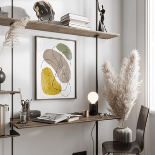 Geometric Abstract Poster print on a wall with natural shapes in muted green, yellow and grey above a desk with an open book