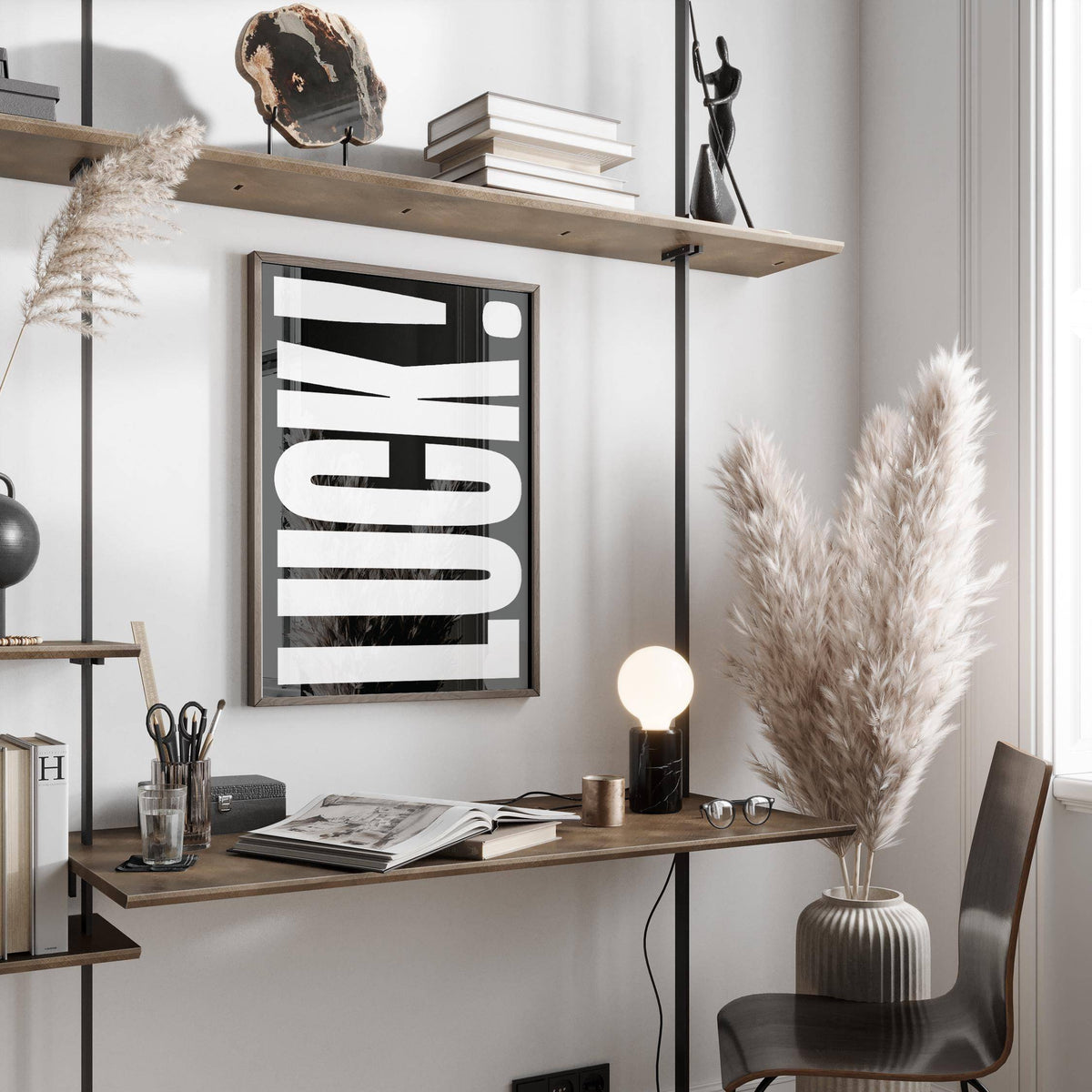 Print on a wall of the typographic word luck in black and white above a desk with books and a lamp