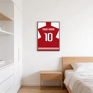 Football shirt poster in red with white sleeves above a wooden bedside table in a bedroom