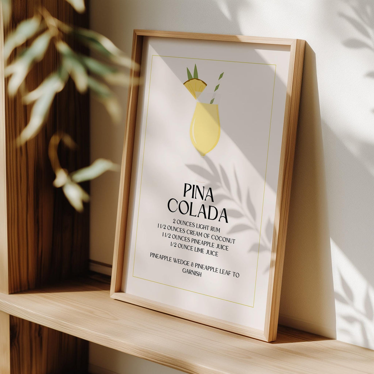 Print leaning on a shelf showing a minimalist pina colada illustration with yellow and green tones and black text