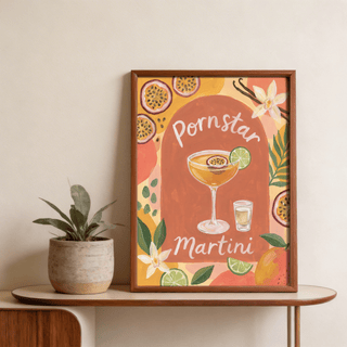 Framed Passion Fruit Martini poster with orange, green and pink watercolour tones on a wooden table with a plant