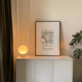 Framed Heart on Map Print leaning on a white cabinet with a lit lamp and plant beside it