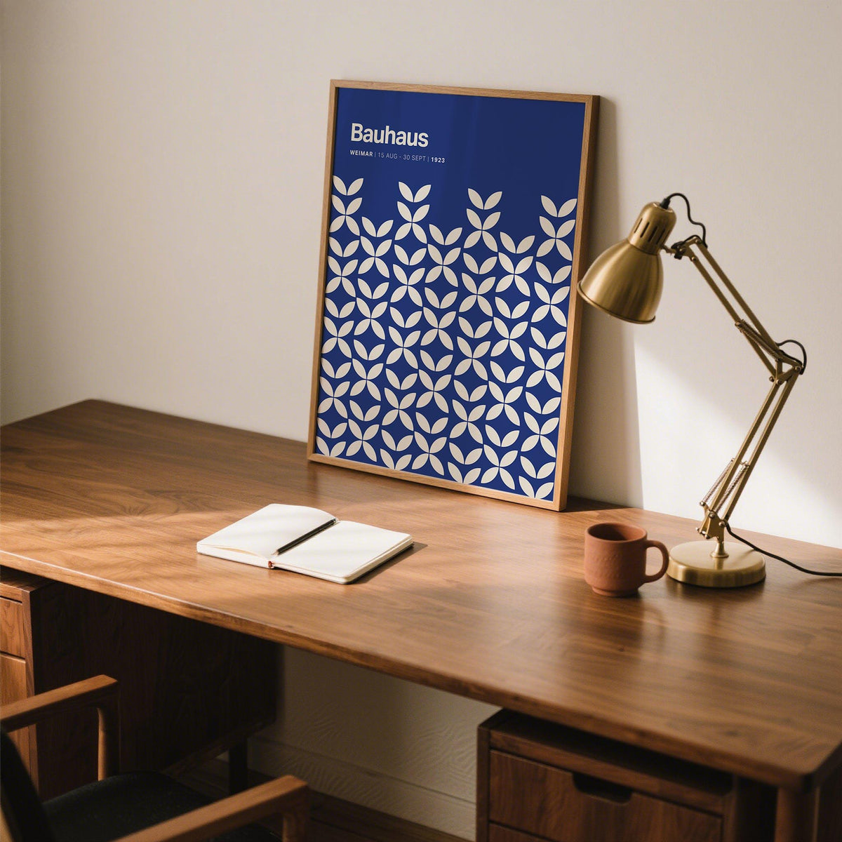 Blue modern wall art with white petal shapes leaning on a wooden desk beside a brass lamp