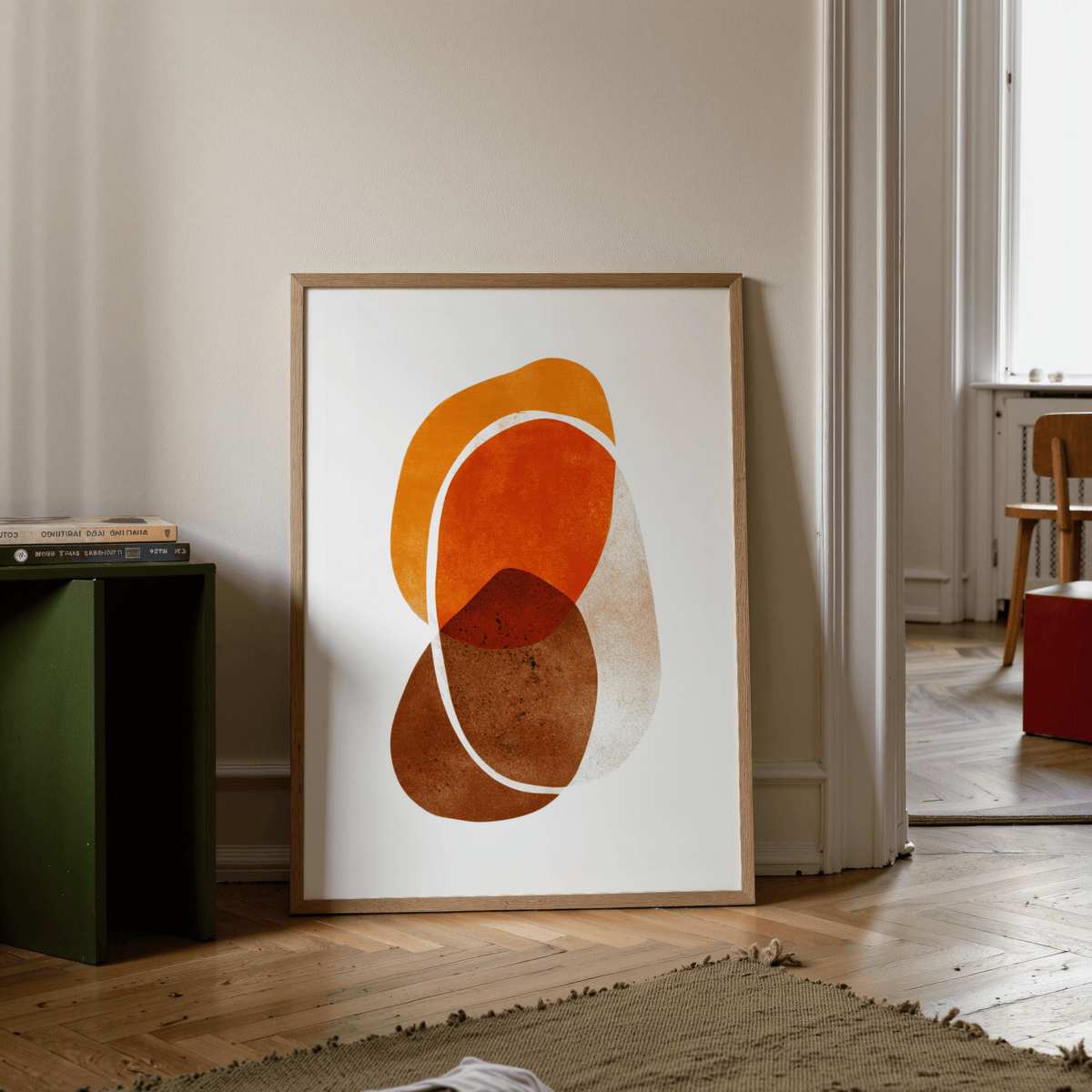 Orange Shapes art print with earthy abstract curves leaning on a wooden floor beside a green stool
