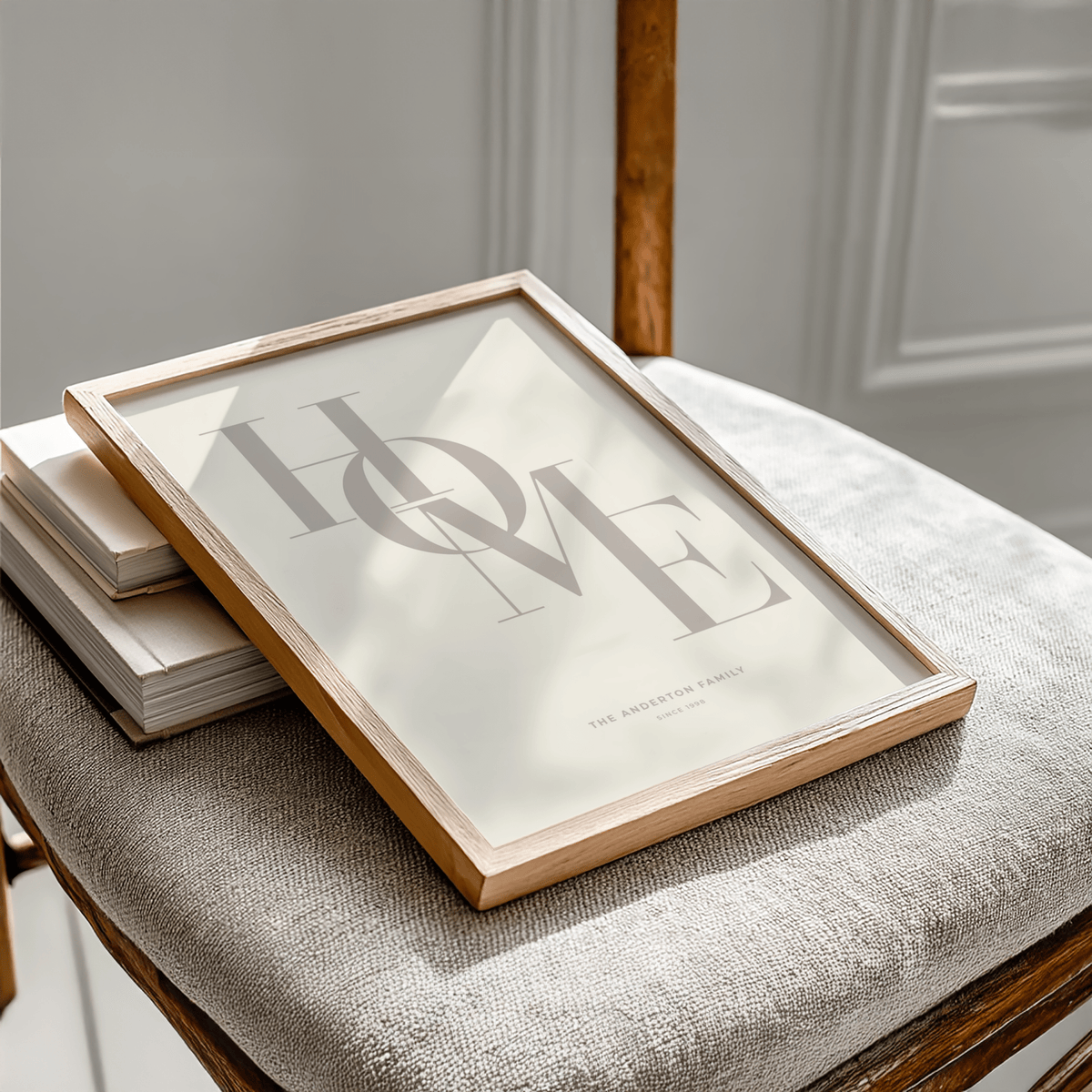 Framed Home Beige Personal Print with minimalist typography leaning on a wooden chair with grey fabric seat