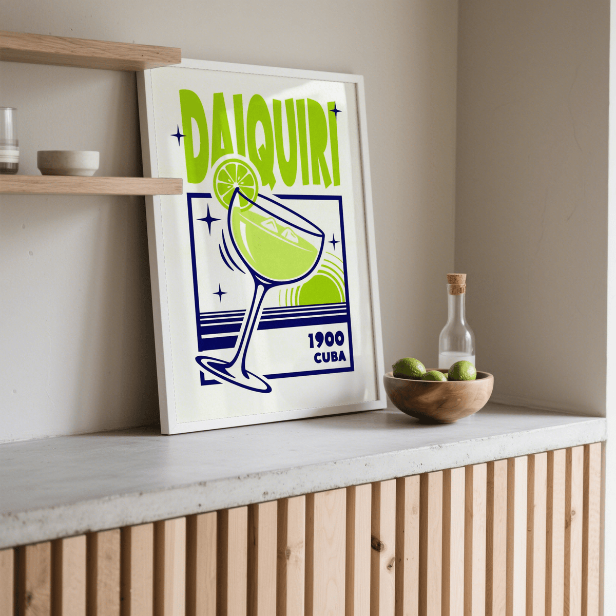 Print leaning on a shelf of a green and blue daiquiri cocktail glass with lime and text, next to a wooden bowl with limes