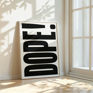 Print leaning on floor of dope typography text in black and white by a glass wall with sunlight