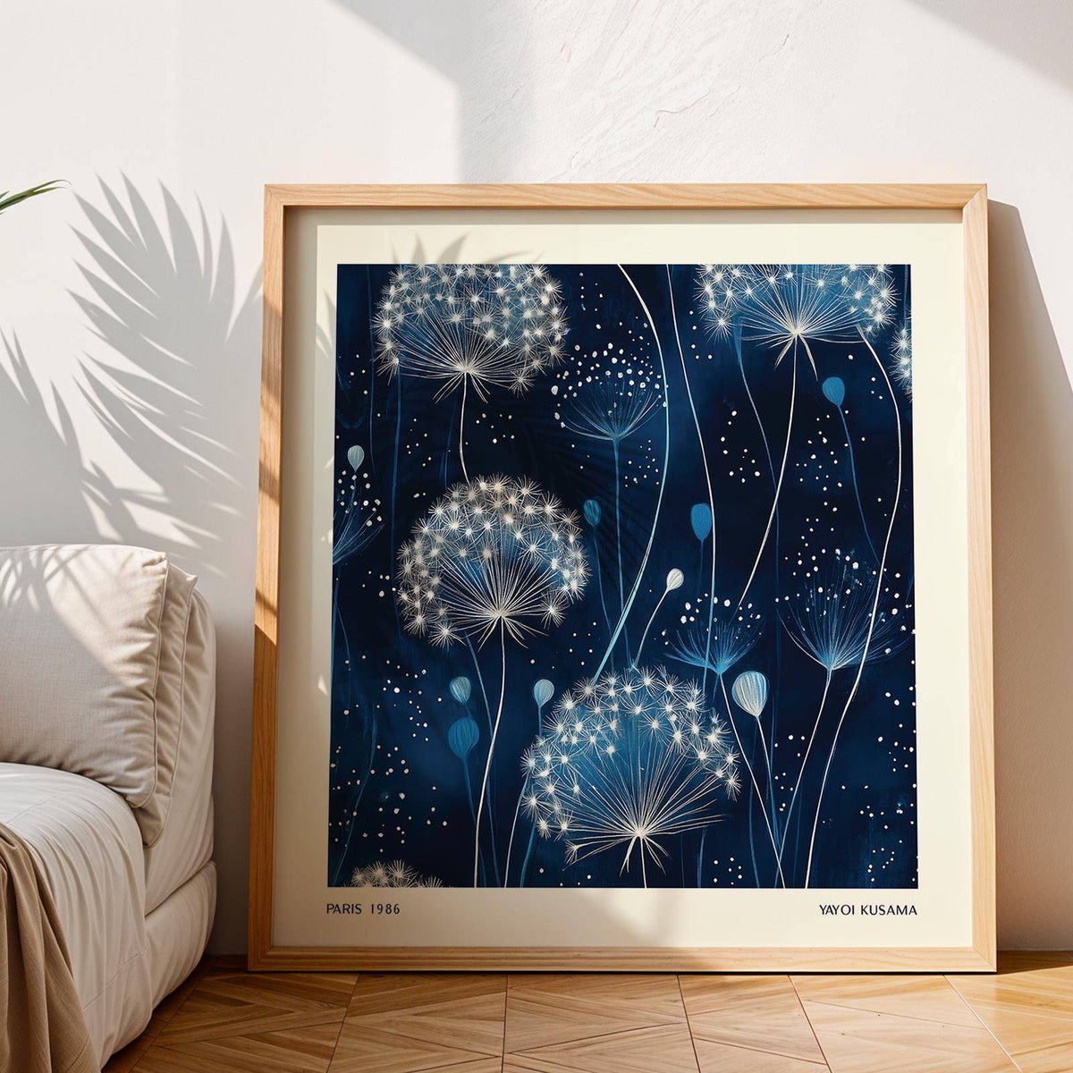 Framed Blue Art Work leaning on floor with dandelion seed heads and natural wood frame near sofa