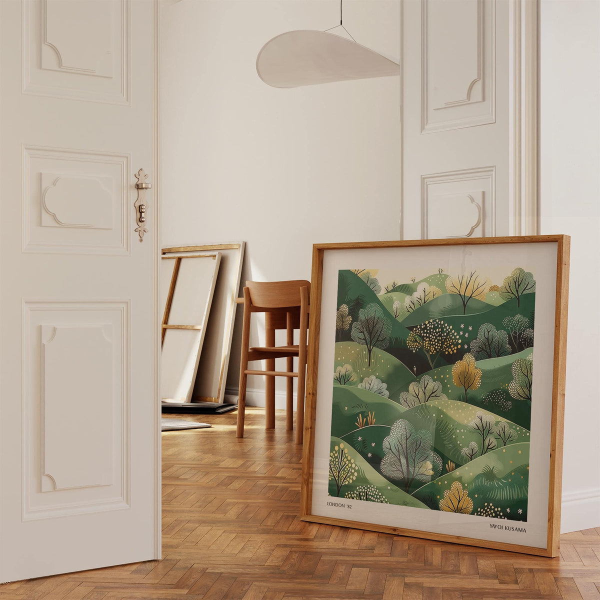 Large nature wall art leaning on floor showing green hills and trees in a minimalist style in a room with parquet flooring