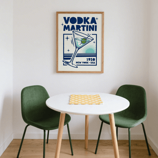 Vodka Martini Poster on a white wall above a small round table with two green chairs in a corner