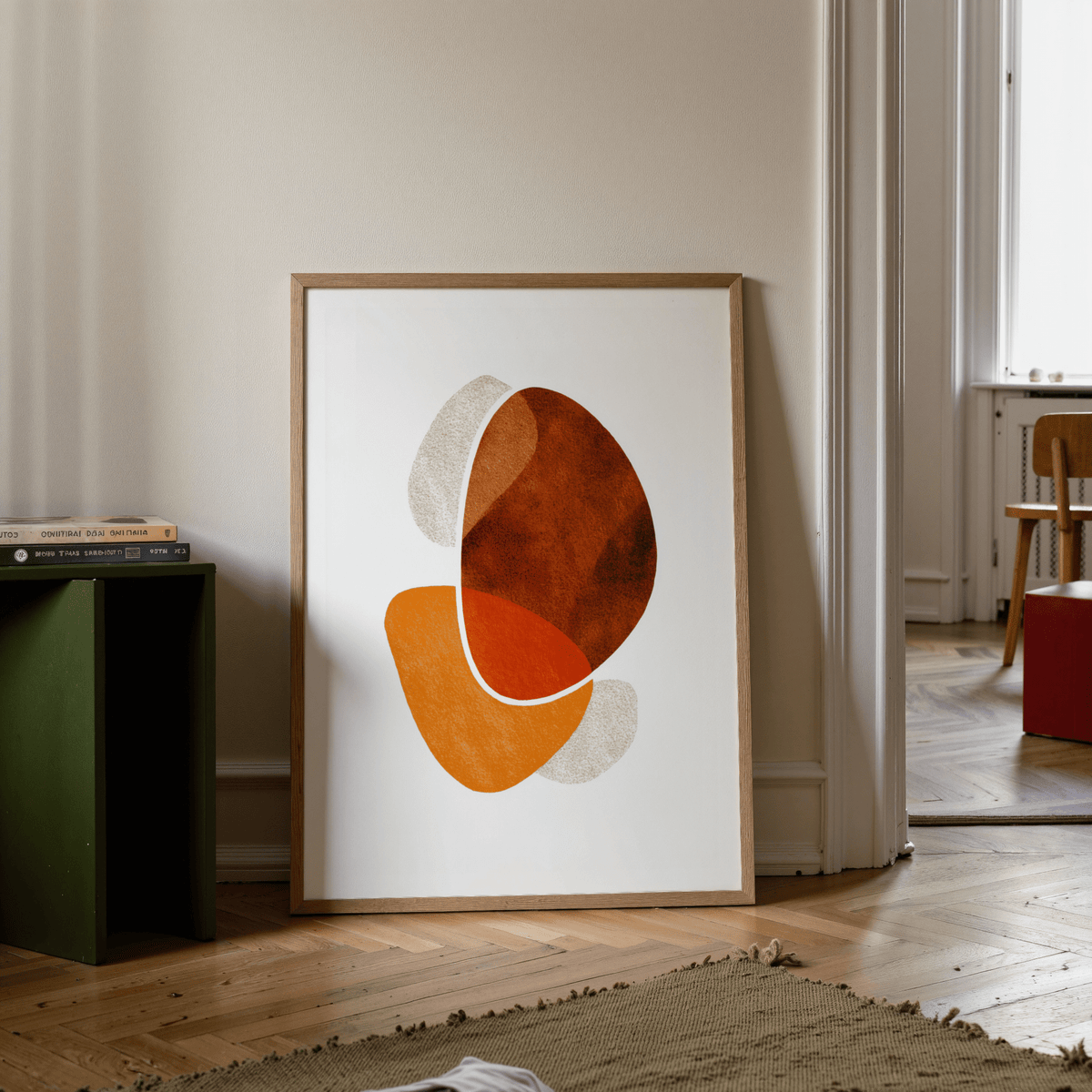 Contemporary abstract poster with orange and brown shapes leaning on a wooden floor near a green side table