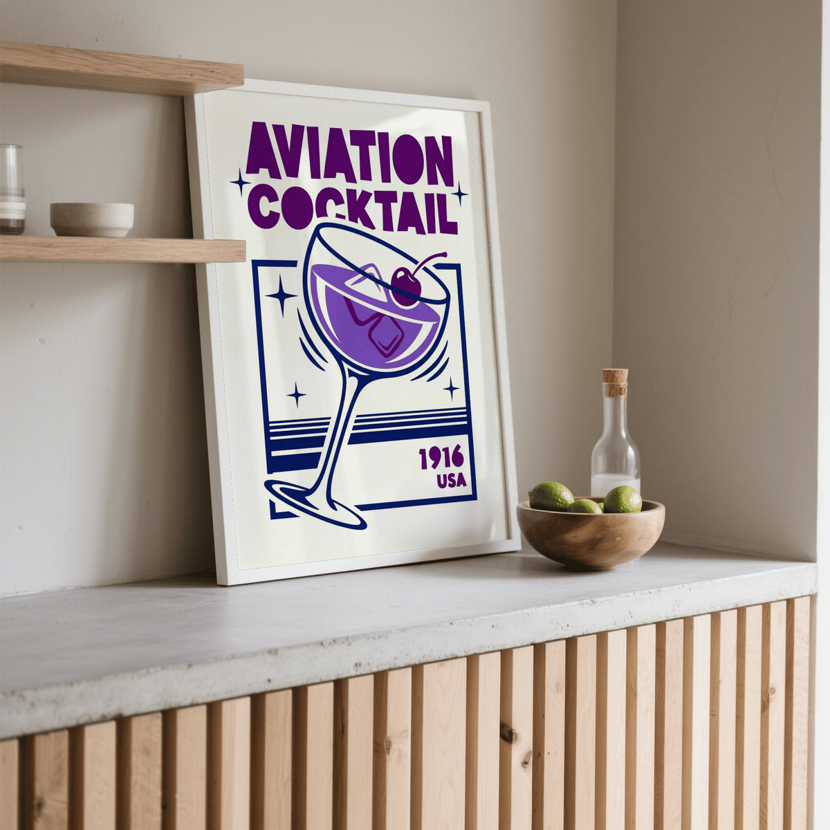 Print leaning on a shelf of an aviation cocktail glass in purple and blue with text above and below and a wooden bowl of limes nearby