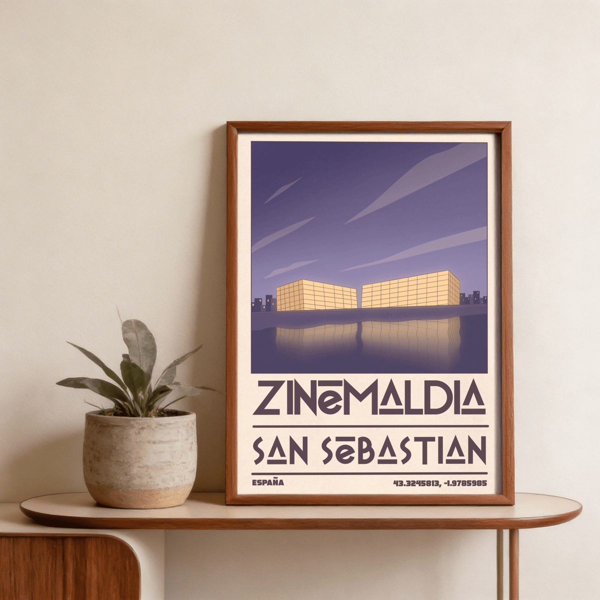 Framed San Sebastian wall art showing minimalist illustration of conference centre buildings with purple sky on a wooden table with plant