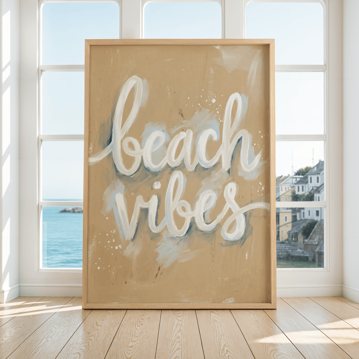 Beach Vibes wall art with white and blue text on sandy background by a large window showing sea and houses
