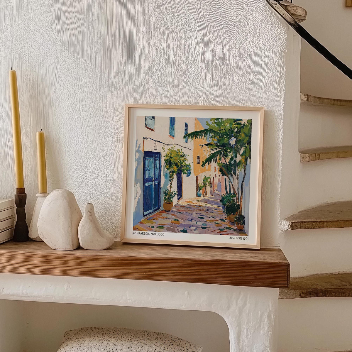 Print leaning on a shelf with Morocco wall art of a Mediterranean street scene in soft blues and greens beside candles