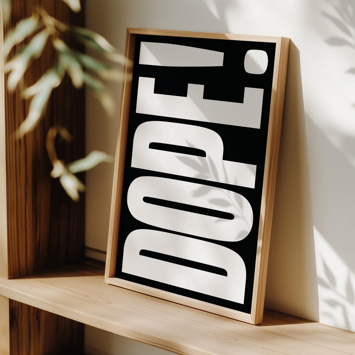 Print leaning on a shelf with dope bold font poster in black and white next to a plant