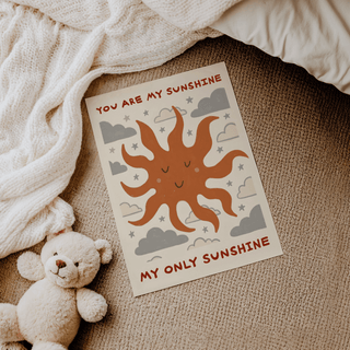 Print of smiling sun illustration with text in brown and grey on beige near a teddy bear on a beige carpet