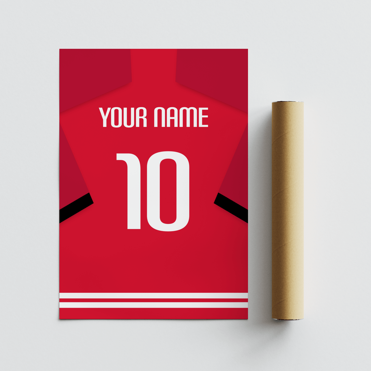 Football shirt poster in red with black sleeve stripe leaning beside a brown packaging tube on a grey surface