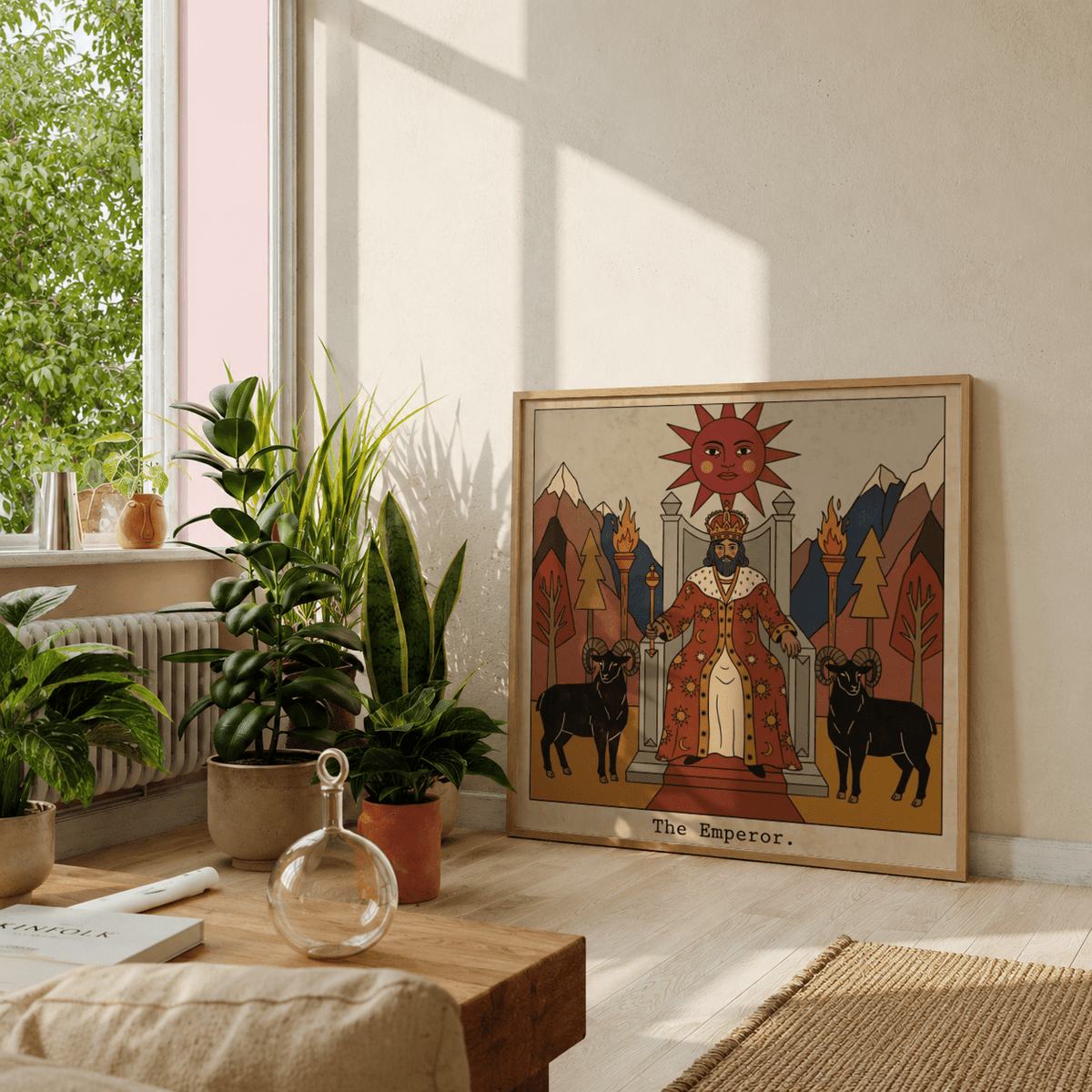 Print leaning on a floor next to green plants showing The Emperor tarot card art with earthy reds and browns