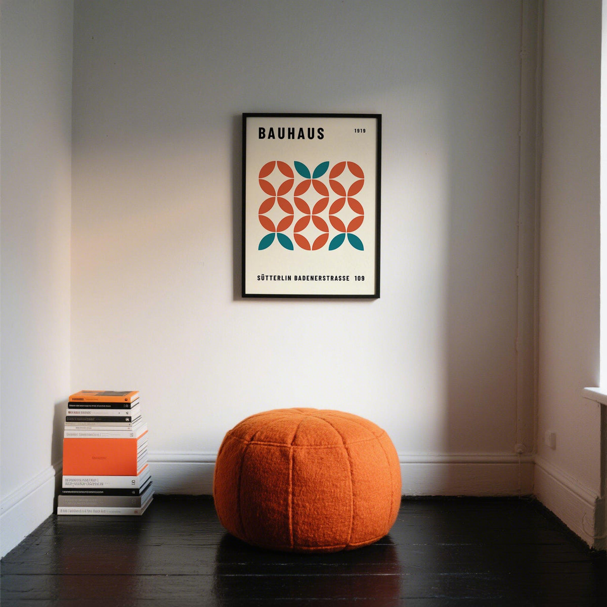 Modern Geometric Wall Art framed print with orange and teal shapes above an orange pouf and stack of books