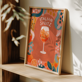 Italian Spritz Art Print leaning on a wooden shelf with shadows and plant leaves nearby
