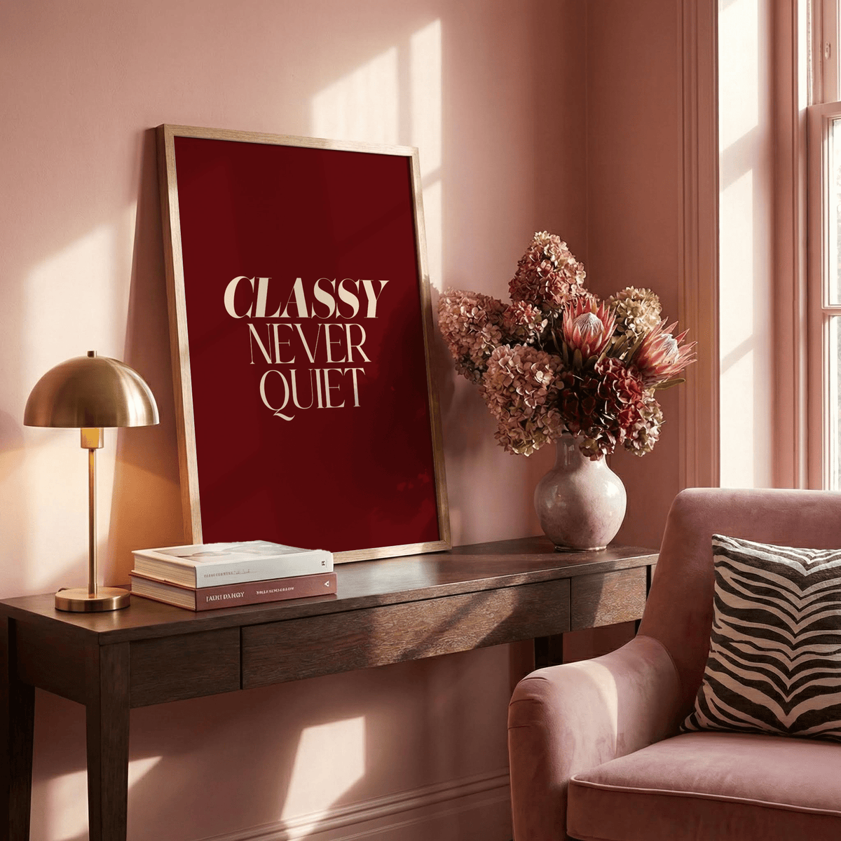 Classy wall art leaning on a wooden sideboard with a vase of dried flowers and lamp nearby